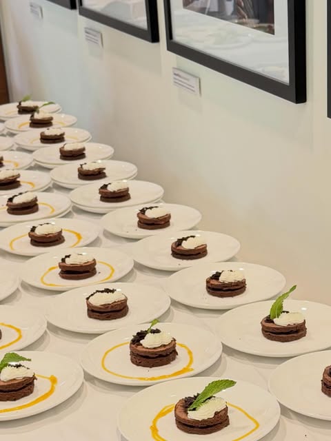 Rows of individually plated round layered desserts with pale topping, green garnish and yellow sauce accents.