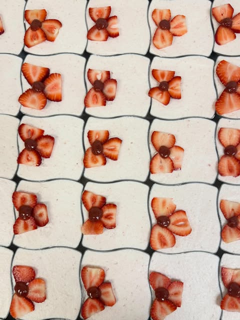 A neatly repeated arrangement of individual desserts in square dishes with sliced-strawberry floral decoration.